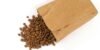 Brown paper bag with aromatic roasted coffee beans spilled on white background.